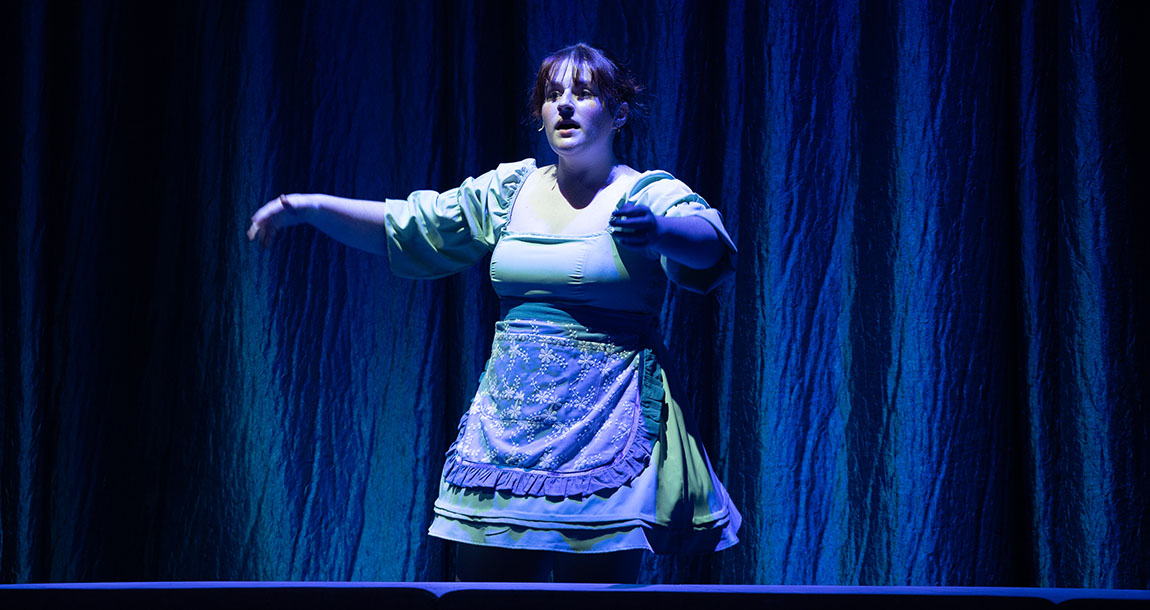 A college student in a green dress costume performs on stage